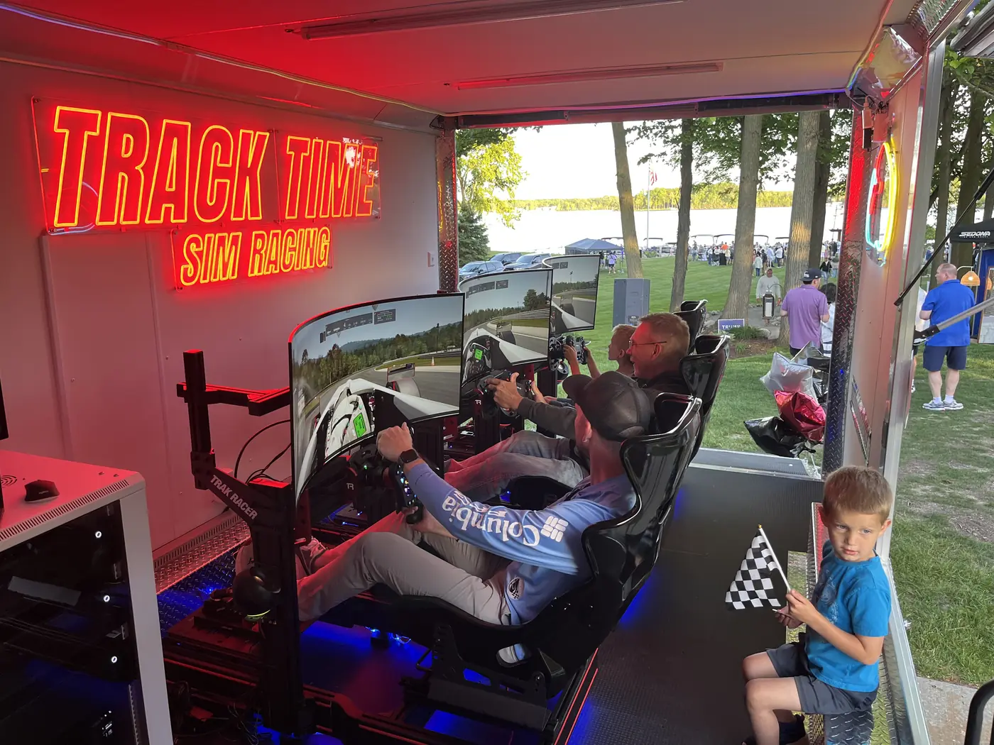 A young racer behind the wheel inside the trailer while a child waves a checkered flag