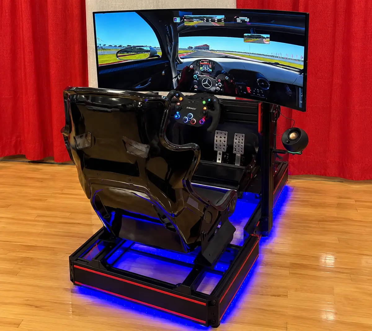A Track Time racing simulator with a curved triple screen, racing seat and blue underglow set up inside a venue